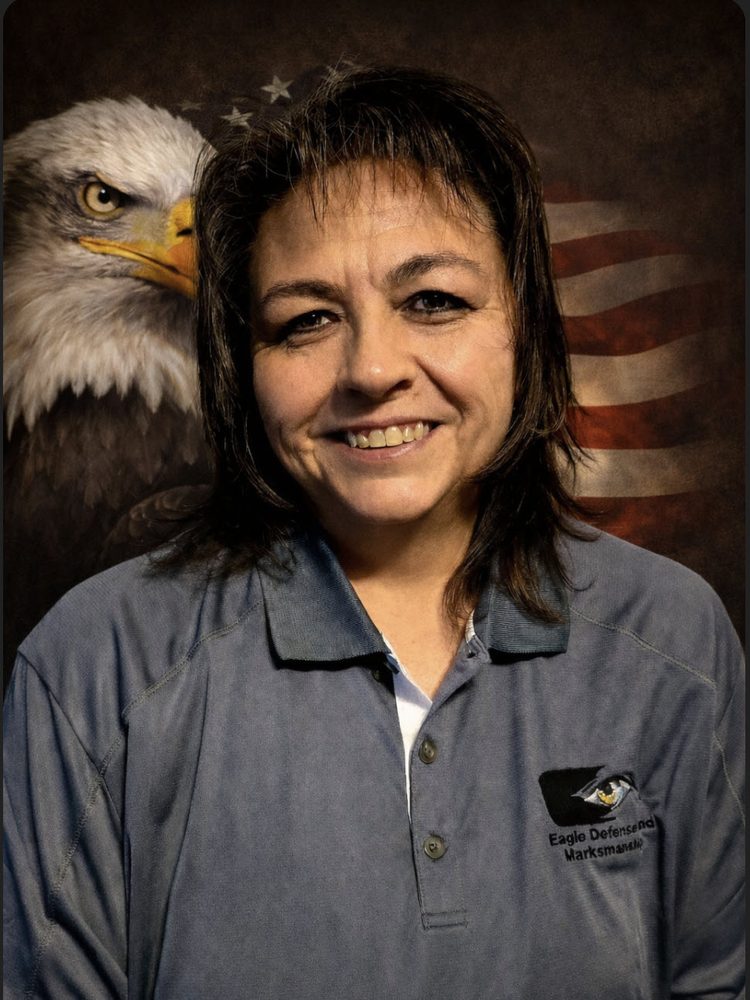Brenda McClellan, Co-Owner and Office Manager at Eagle Defense and Marksmanship, smiling in front of an American flag and bald eagle backdrop